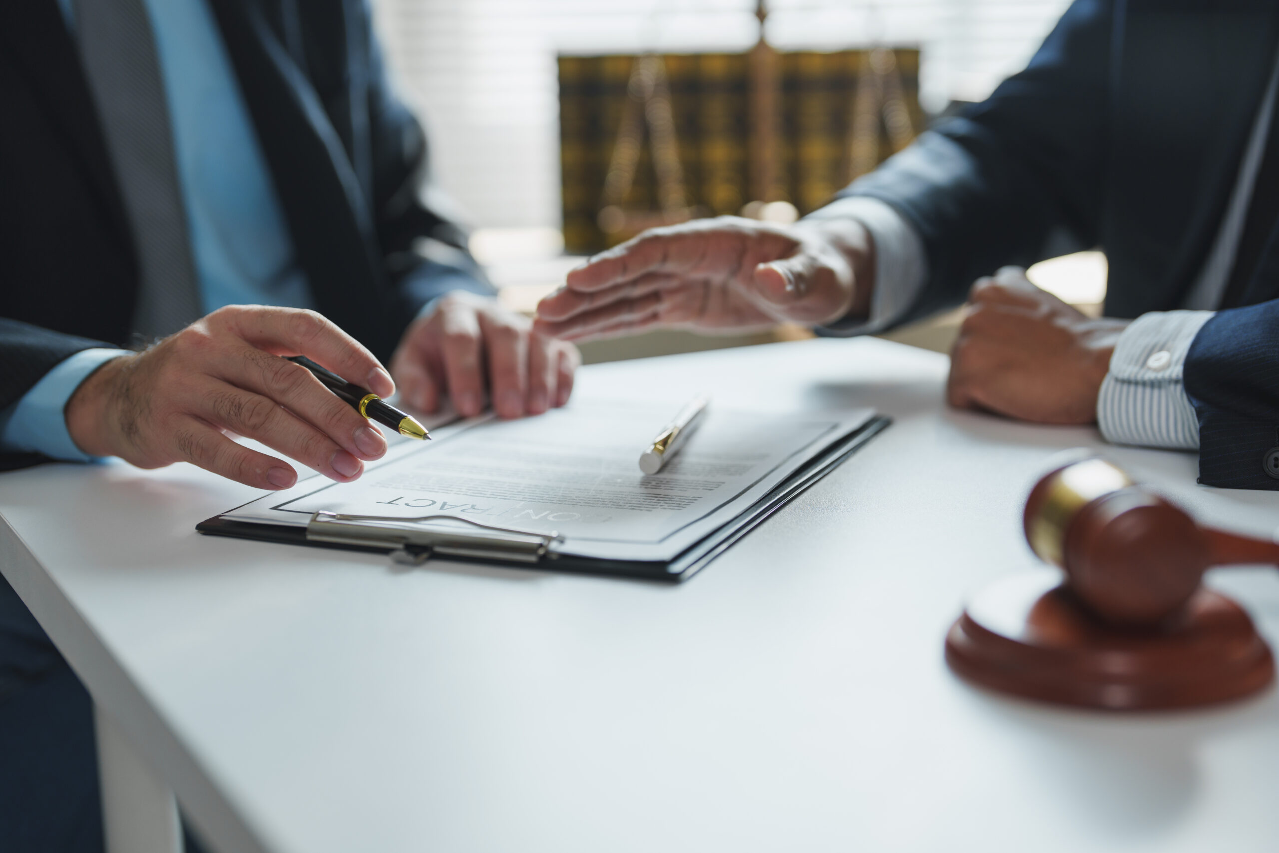 Deux professionnels discutant d’un contrat juridique avec un document et un marteau de juge en premier plan, représentant un service de conseil juridique en entreprise