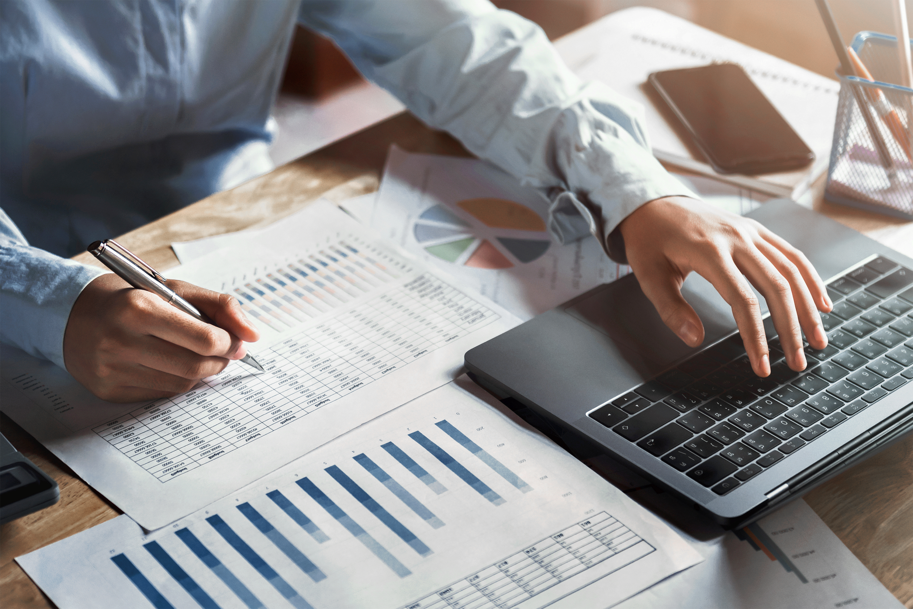 Employé saisissant des données sur un ordinateur portable entouré de graphiques et documents administratifs, illustrant le support administratif en entreprise